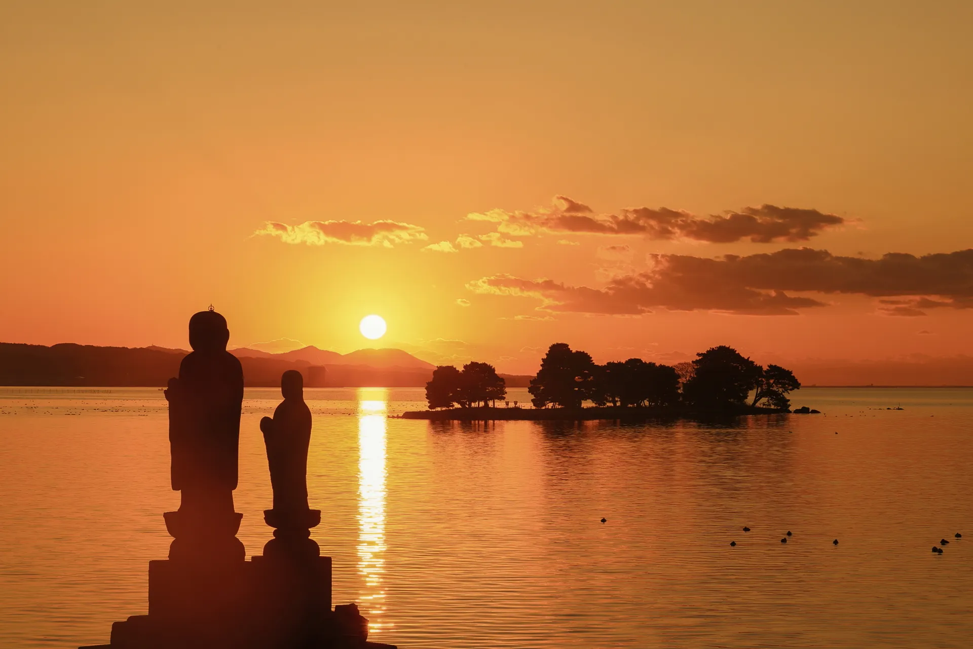 Jizō-Figuren am Ufer des Shinji-Sees bei Sonnenuntergang, dahinter die Insel Yomegashima